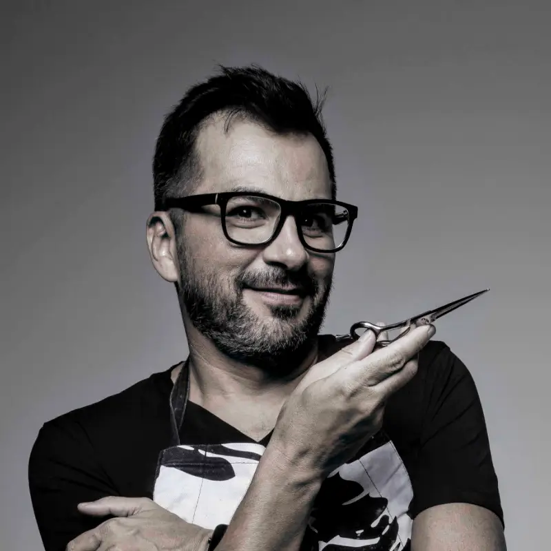 Luciano Boy, cabeleireiro visagista e educador do Beauty.co.lab, segurando uma tesoura em gesto simbólico de transformação e arte capilar.