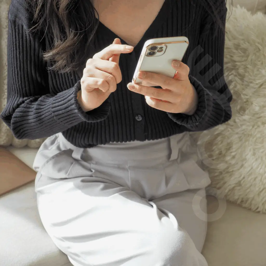 Mulher elegante sentada confortavelmente em um ambiente acolhedor, sorrindo enquanto faz um agendamento pelo celular em um espaço de beleza.