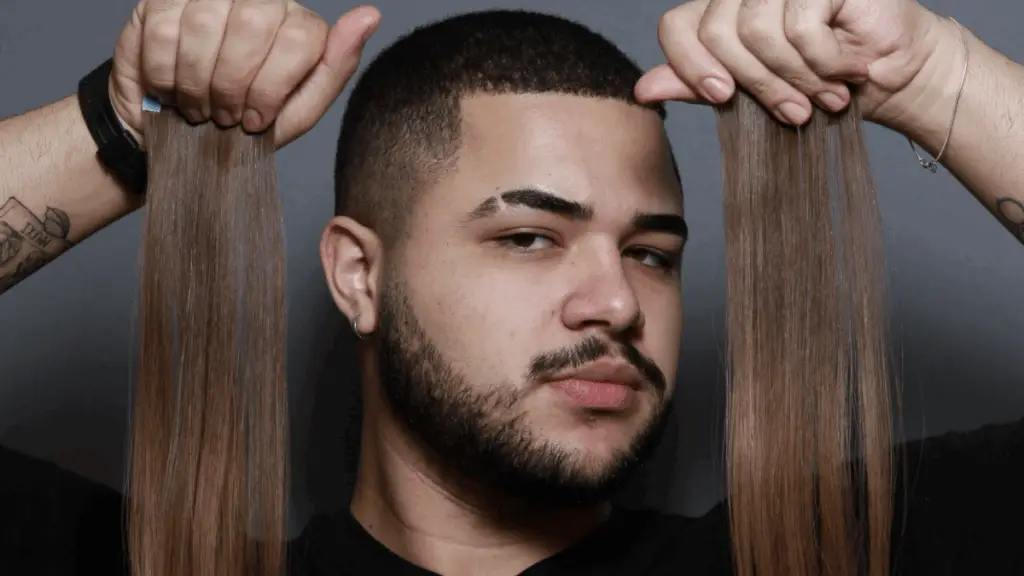 Davi Moraes segura mechas de extensões capilares com expressão confiante, pronto para aplicar em um processo de transformação no salão Beauty.co.lab.