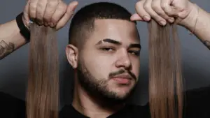 Davi Moraes segura mechas de extensões capilares com expressão confiante, pronto para aplicar em um processo de transformação no salão Beauty.co.lab.