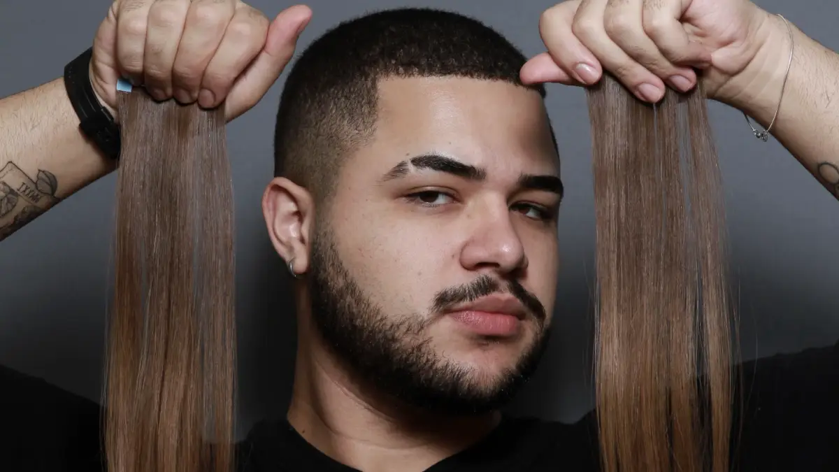Davi Moraes segura mechas de extensões capilares com expressão confiante, pronto para aplicar em um processo de transformação no salão Beauty.co.lab.