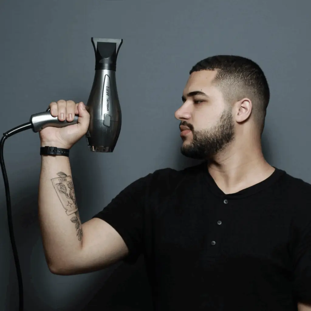Davi Moraes posa de perfil com expressão séria e confiante, empunhando um secador de cabelo apontado para cima.