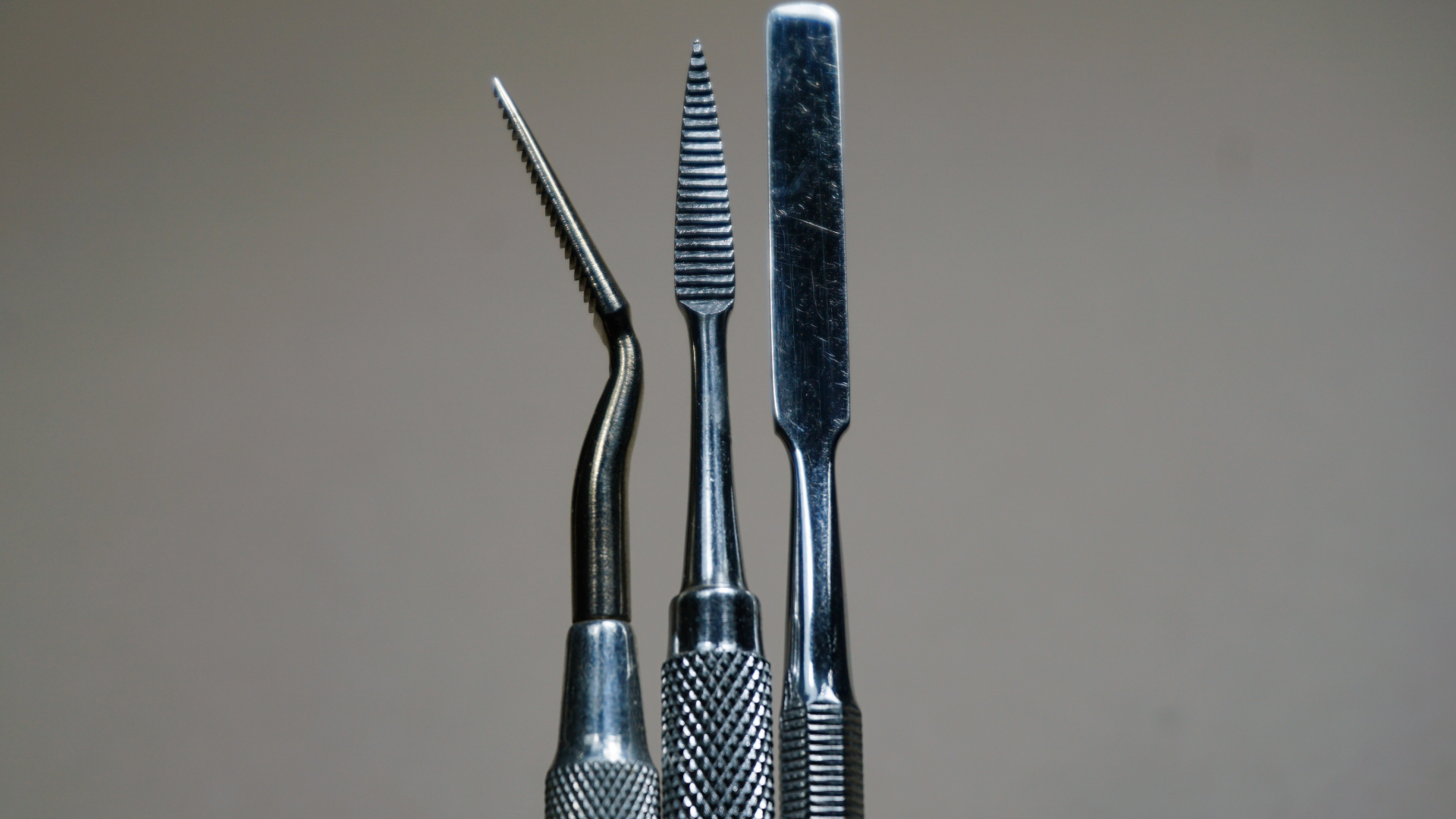 Três instrumentos metálicos de podologia sobre superfície limpa, prontos e esterilizados para atendimento